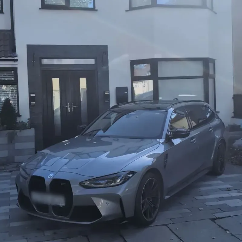 A grey BMW G81 M3 Touring outside a house